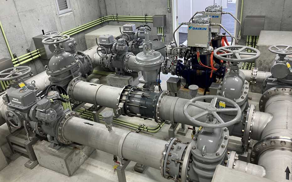 東洋鋼鈑下松事業所に設置されたマイクロ水力発電設備の内部。バルブや電動弁が組み込まれた工業用水配管システムと、その奥に鎮座する「DAIKIN」ロゴ入りの縦型マイクロ水力発電機(小水力発電機)。