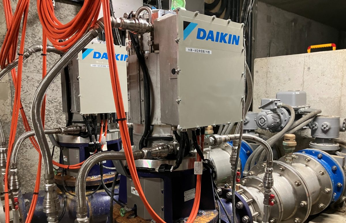 ダイキン(DAIKIN)のロゴと「水車一体型発電機」の銘板が見える、地下に設置された縦型マイクロ水力発電機のアップ写真