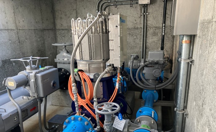 地下ピット(流入弁室)内に収められたマイクロ水力発電機。青い配管や電動弁と接続され、縦型・省スペース設計を活かして垂直に据え付けられている様子。既存施設の狭小空間に収まることを裏付けている。