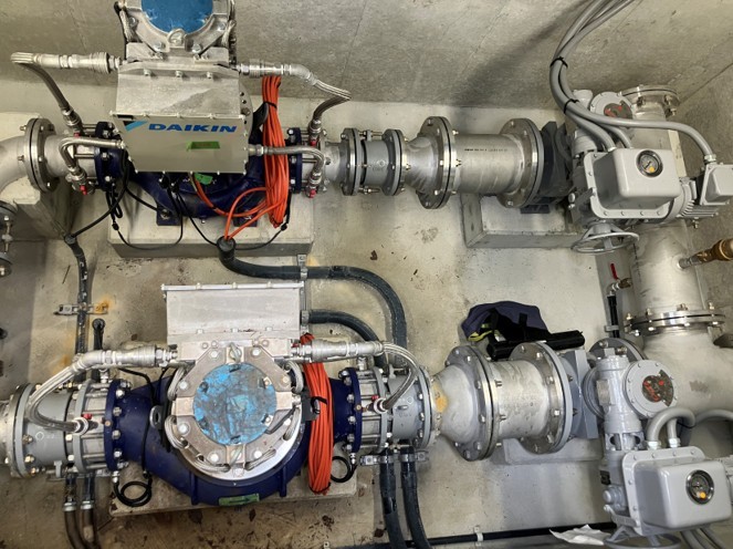 吹田市津雲配水場の地下ピット内に2台並列で据え付けられたDAIKINブランドのマイクロ水力発電機と周辺配管の俯瞰写真
